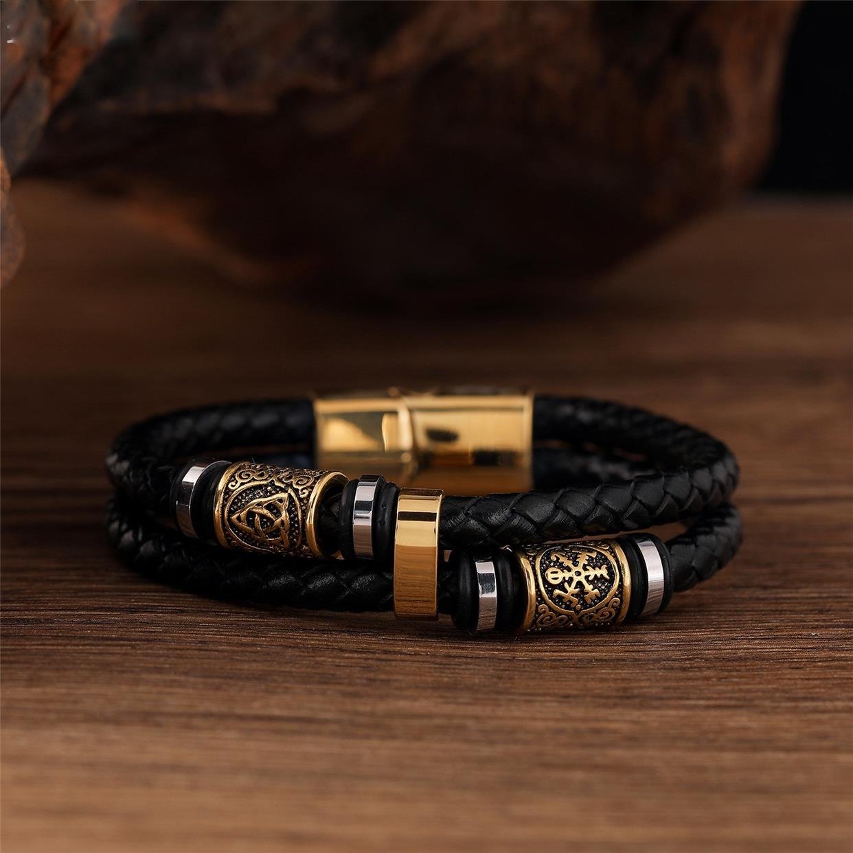 Black braided leather bracelet with gold and bronze metal beads on a wooden surface
