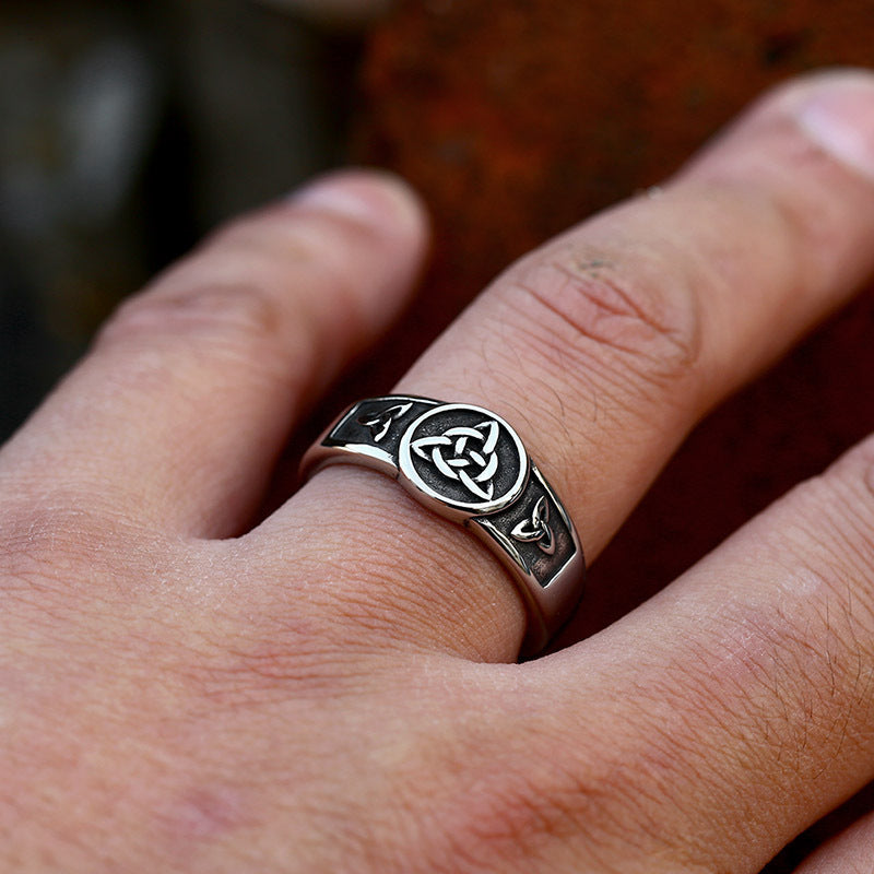 Silver ring with Celtic knot design worn on a finger against a blurred background