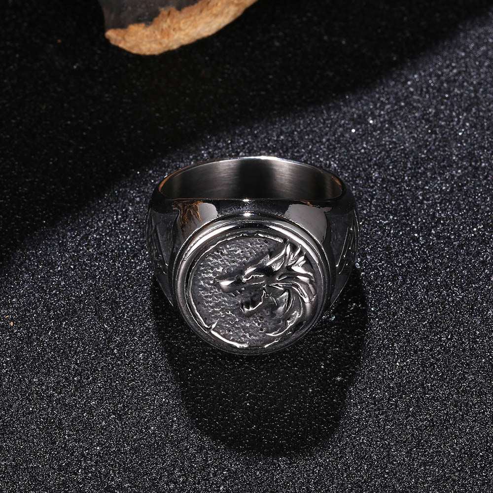 Silver ring with dragon emblem on a black textured surface