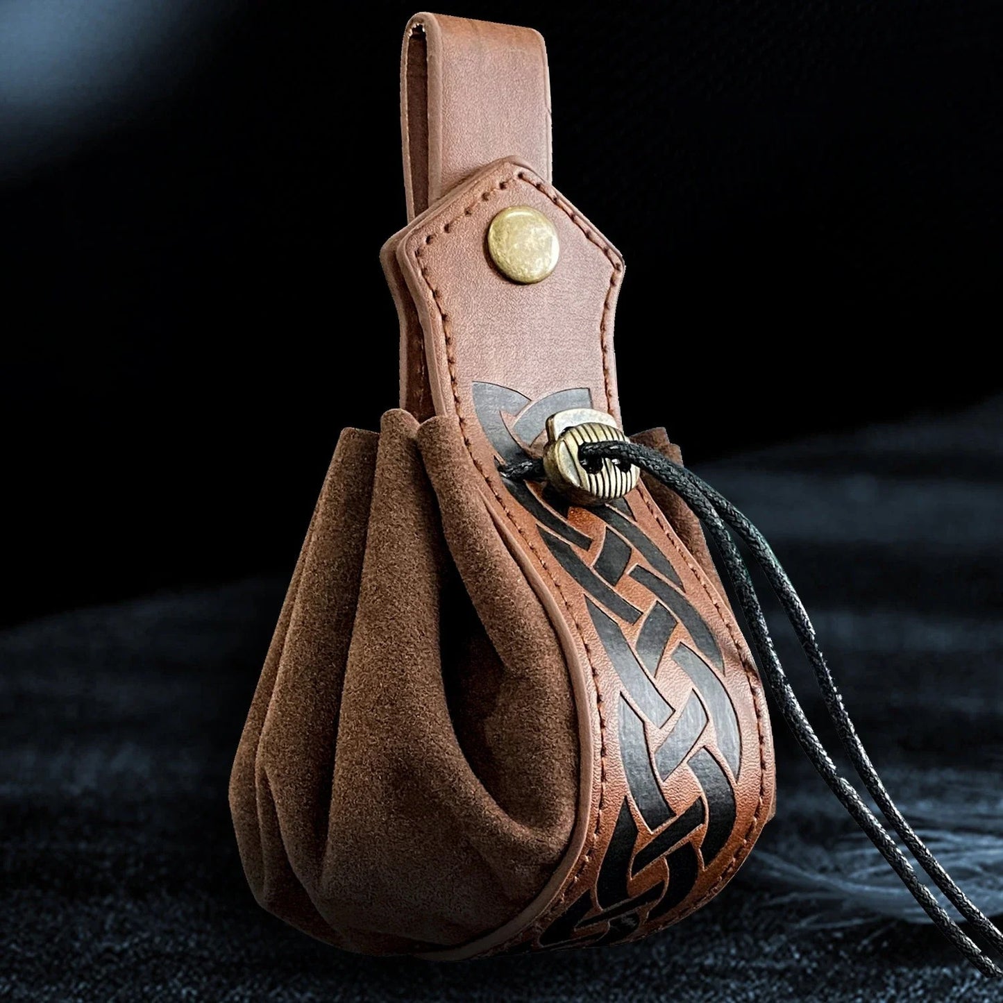 Brown leather pouch with decorative pattern and button on a dark background