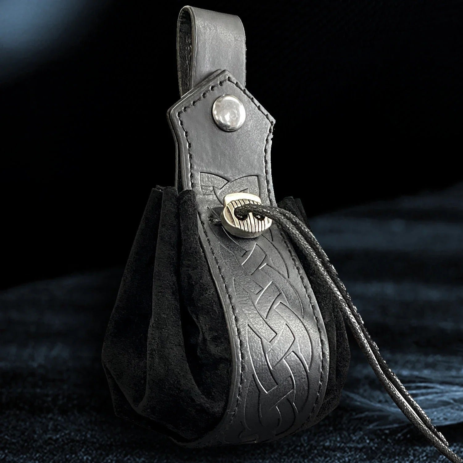 Black leather pouch with intricate design and button closure on a dark background