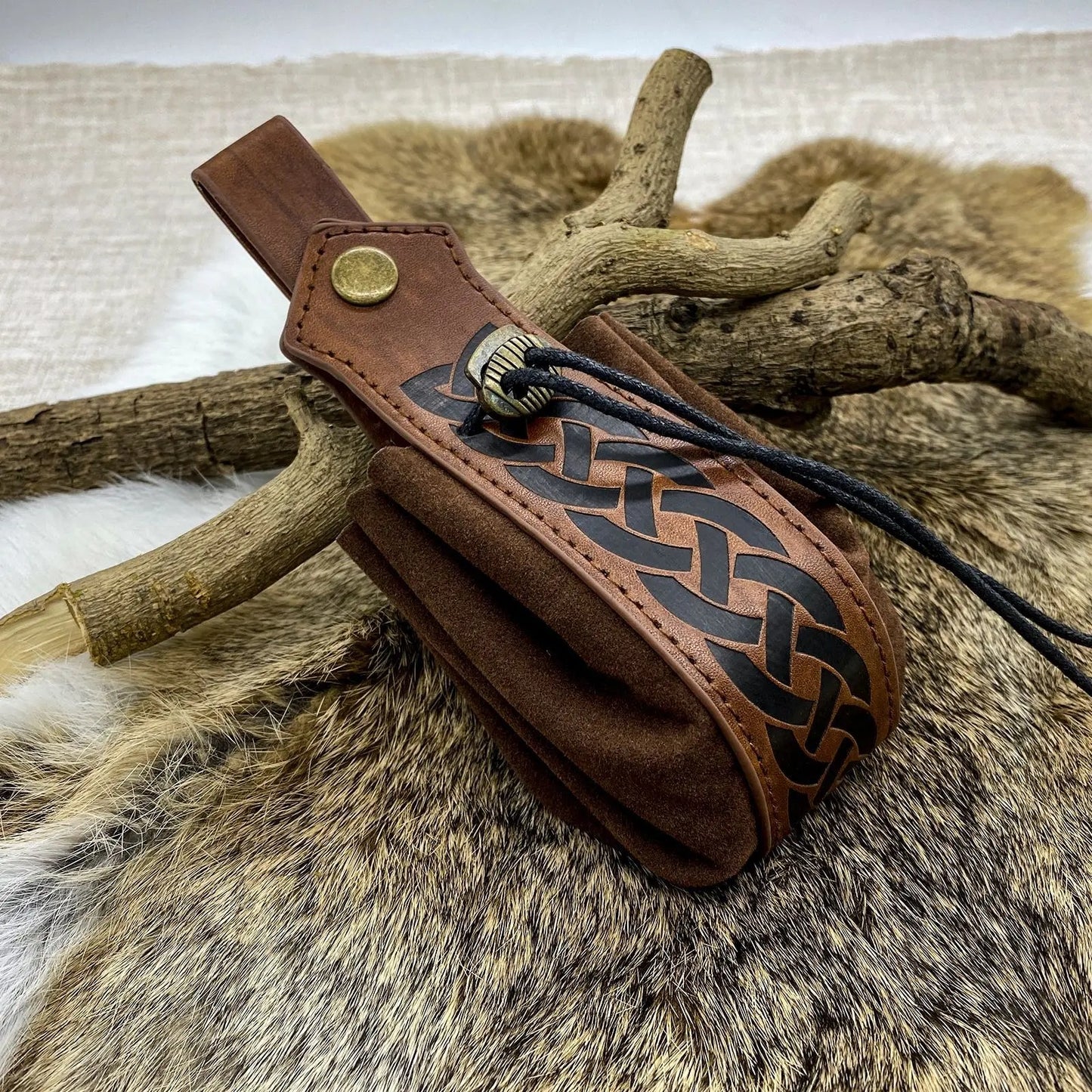 Brown leather quiver with decorative braiding on a fur and wood background