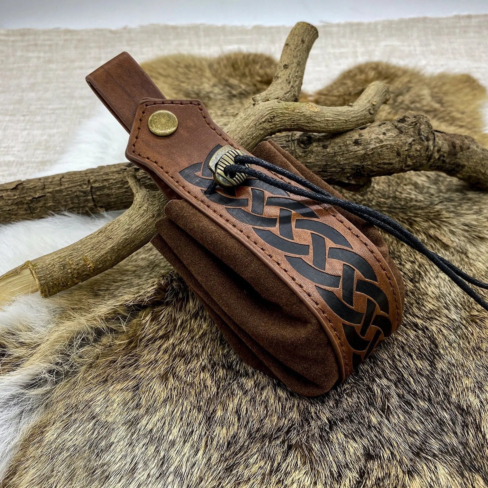 Brown leather quiver with decorative braiding on a fur and wood background