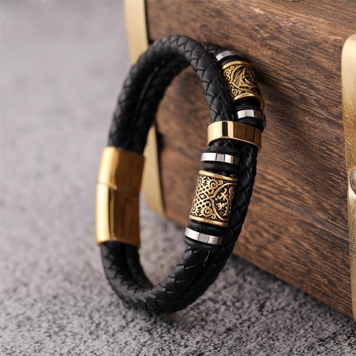 Black braided leather bracelet with gold and silver metal accents on a wooden surface.