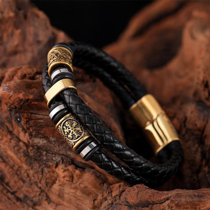 Black braided leather bracelet with gold and silver accents on a wooden surface